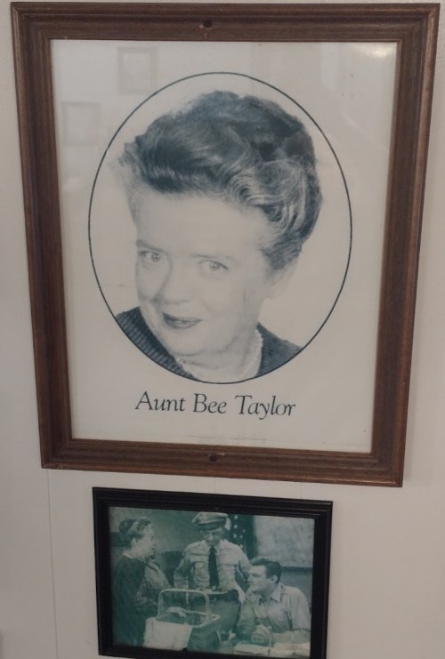 Framed portrait of Aunt Bee Taylor, featuring a woman with styled hair and a friendly expression, displayed on a wall.