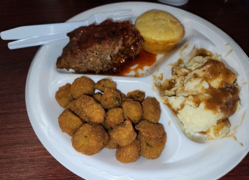 A plate with meatloaf, cornbread muffin, mashed potatoes with gravy, and fried okra.