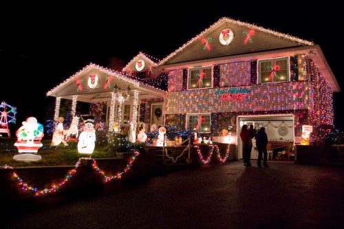 A brightly lit house decorated for Christmas with colorful lights, festive figures, and a snowy scene at night.