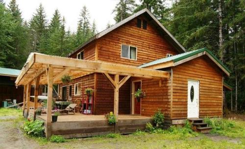 A rustic wooden house with a porch, surrounded by tall trees and greenery.