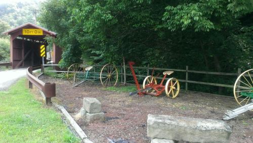 A rustic scene featuring old wooden wheels and a covered bridge surrounded by greenery.