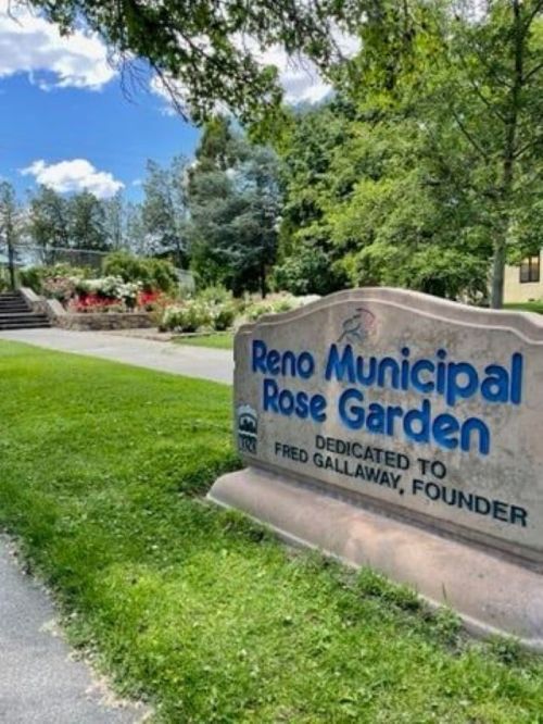 Sign for the Reno Municipal Rose Garden, dedicated to founder Fred Galloway, surrounded by greenery and flowers.