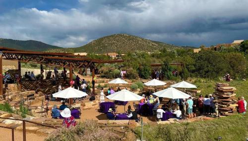 Outdoor event with guests under umbrellas, surrounded by greenery and mountains, set against a cloudy sky.