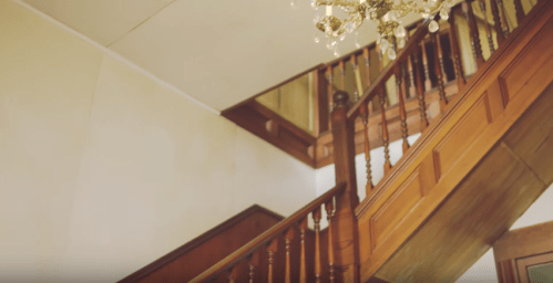 A wooden staircase with a chandelier, leading to an upper level in a well-lit interior space.