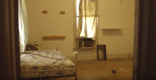 A sparse room with a bed, window, and air conditioner, featuring bare walls and minimal furnishings.