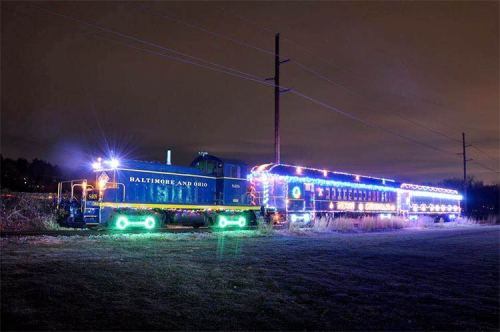 A brightly lit train with colorful lights parked on a track at night, surrounded by dark fields.