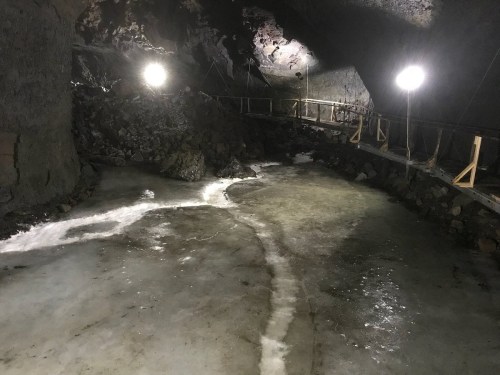 A dimly lit underground cave with icy ground and rocky walls, featuring wooden walkways and bright lights.