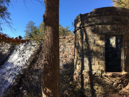 A stone structure beside a waterfall, surrounded by trees and blue sky.