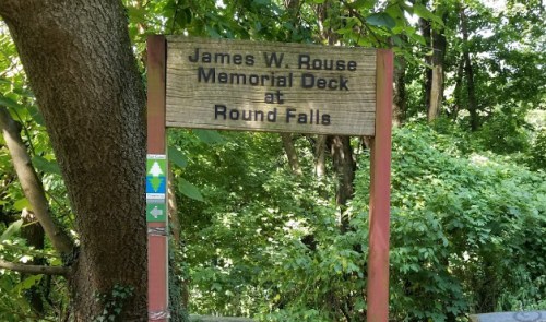 Sign for the James W. Rouse Memorial Deck at Round Falls, surrounded by lush greenery.