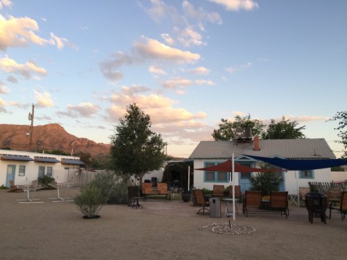 A serene outdoor area with seating, trees, and a mountain backdrop under a blue sky with scattered clouds.