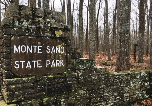 Stone sign for Monte Sano State Park surrounded by bare trees and a forest floor covered in leaves.