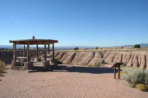 A wooden gazebo overlooks a rugged landscape of colorful rock formations under a clear blue sky.