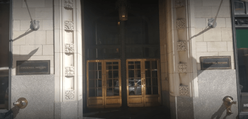 Entrance of a building featuring ornate doors and decorative stonework, with plaques on either side.