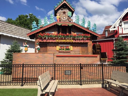 A charming wooden building with a clock, decorated with flowers and trees, surrounded by benches and a fence.