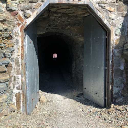 A stone archway with metal doors leads into a dark tunnel, surrounded by rocky terrain.