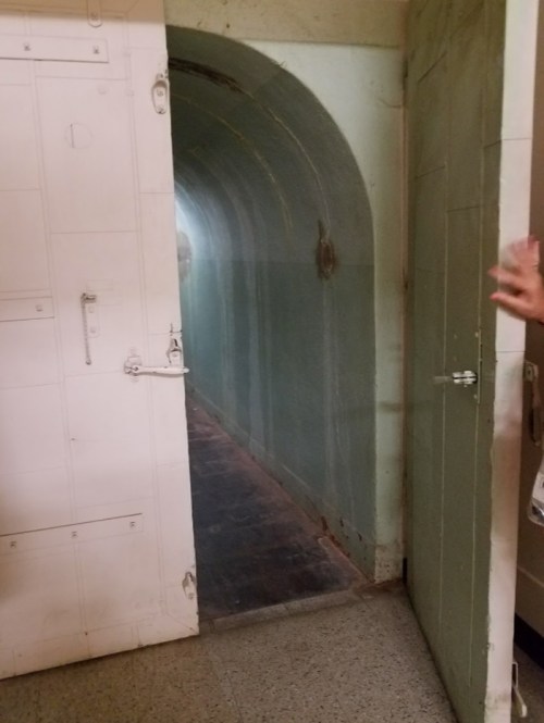 A narrow, arched hallway with a light green wall, partially obscured by a white door being opened.