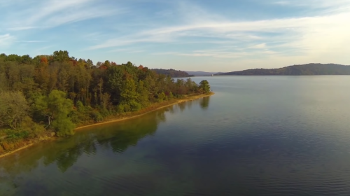 A serene lakeside view with trees lining the shore and calm waters reflecting the sky.