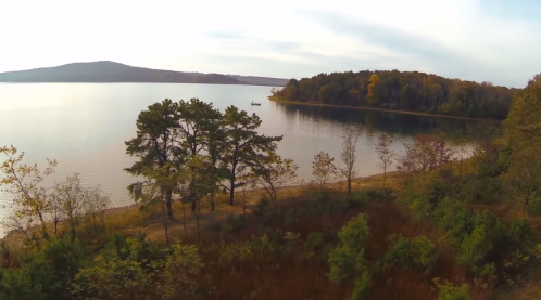 A serene lake scene with trees along the shore and a boat in the distance, surrounded by autumn foliage.