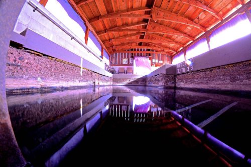 A tranquil indoor pool with wooden beams overhead, reflecting light on the water's surface.