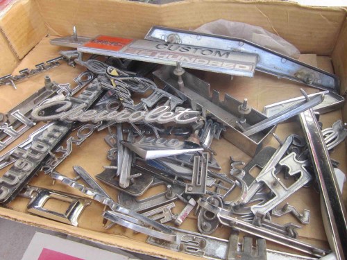 A box filled with various vintage car emblems and badges, including "Custom" and "Chevrolet" logos.