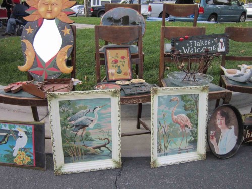 A collection of vintage items, including framed artwork, a decorative sun, and a "Welcome" sign, displayed on chairs.