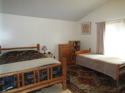 Cozy bedroom with two wooden beds, a dresser, a lamp, and a bookshelf, featuring warm colors and a rug.