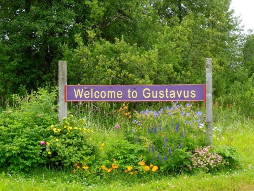 A colorful sign reading "Welcome to Gustavus" surrounded by lush greenery and vibrant flowers.