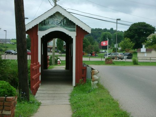A red covered bridge with a painted mural leads to a road, featuring a Swiss flag in the background.