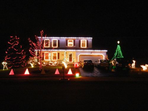 A house decorated with colorful Christmas lights, featuring a tree, reindeer, and festive shapes in the yard at night.