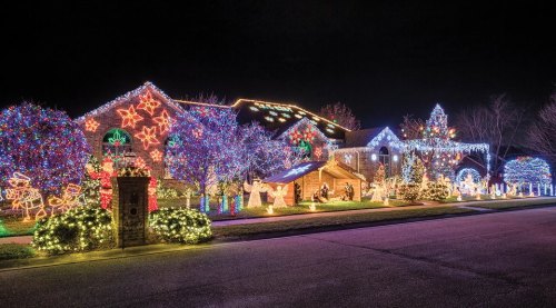 A beautifully decorated house with colorful Christmas lights, trees, and festive displays glowing at night.