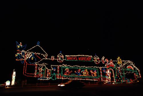 Colorful holiday lights illuminate a large building labeled "Santa's Workshop" against a dark night sky.