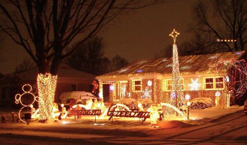 A beautifully decorated house with colorful Christmas lights, snow on the ground, and festive displays in the yard.