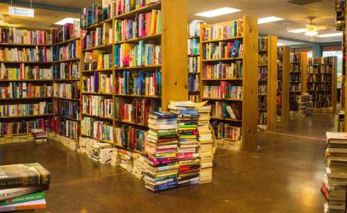 A cozy bookstore with tall shelves filled with colorful books and stacks of books on the floor.