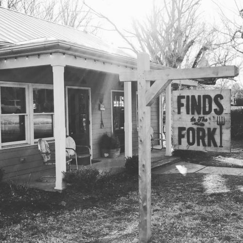 A rustic building with a sign reading "Finds by the Fork," surrounded by trees and a sunny atmosphere.