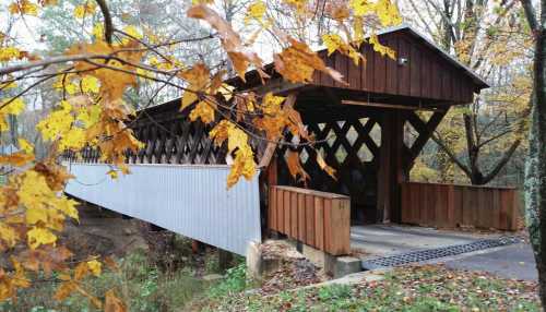 A wooden covered bridge surrounded by autumn leaves and trees, spanning a small creek.