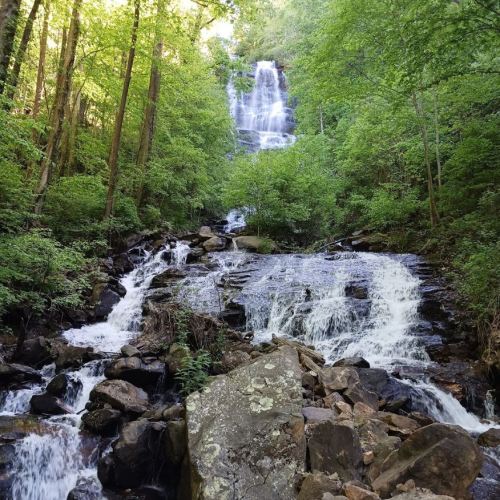 A serene waterfall cascades down rocky terrain, surrounded by lush green trees and foliage.
