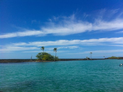 A serene tropical scene featuring turquoise water, a small island with palm trees, and a clear blue sky with clouds.