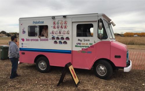 A colorful ice cream truck with a menu displayed on the side, parked in a field with a person standing nearby.