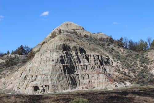 A rugged, layered hill with a blue sky above and sparse vegetation surrounding it.