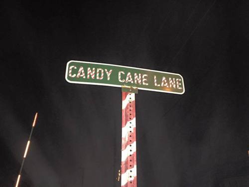 A street sign reading "Candy Cane Lane" illuminated at night, with a festive design.