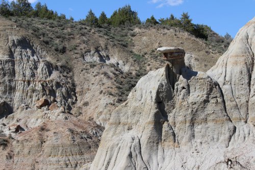 A rocky landscape featuring a prominent, flat-topped rock formation against a backdrop of hills and blue sky.