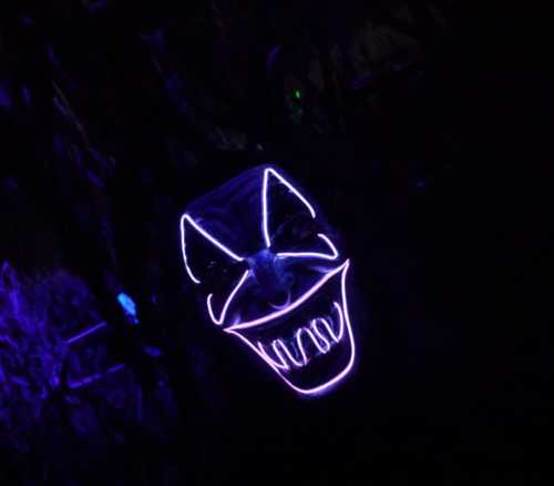 A glowing mask with a sinister smile, outlined in neon purple light against a dark background.