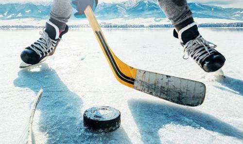 A hockey player skates on ice, poised to shoot a puck with mountains in the background.