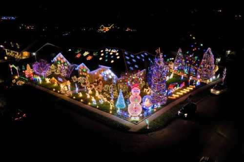 Aerial view of a brightly lit yard decorated with colorful Christmas lights, trees, and festive displays.