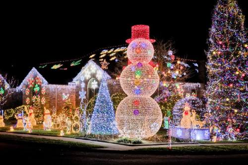 A festive display featuring a large illuminated snowman, decorated trees, and colorful lights on a house at night.