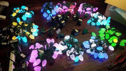 Colorful string lights in various shapes scattered on a table, glowing in shades of blue, green, purple, and white.