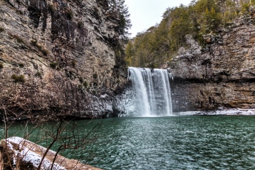 A serene waterfall cascades into a turquoise pool, surrounded by rocky cliffs and lush greenery.