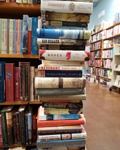 A stack of books on a shelf in a bookstore, featuring various titles and authors.