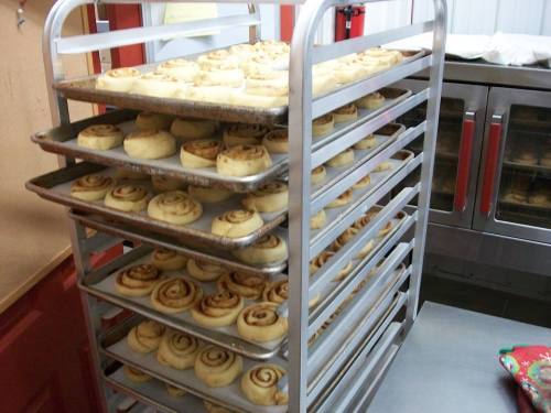 A metal rack filled with trays of uncooked cinnamon rolls, ready for baking in a kitchen setting.