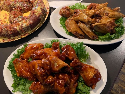 Two plates of chicken wings on lettuce: one with BBQ sauce, the other plain, alongside a colorful dessert.